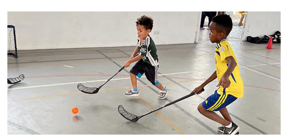 Two young students playing floorball with sticks and a ball during a Hockey Jams PE lesson